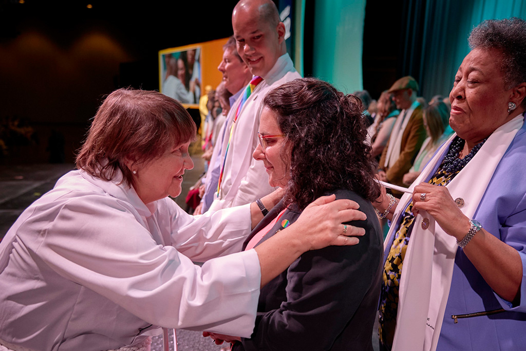 Bishop Karen Oliveto consecrates Maria Capezio Crookes as a deaconess during the 2022 United Women in Faith Assembly. Deaconess Clara Ester stands behind her.
