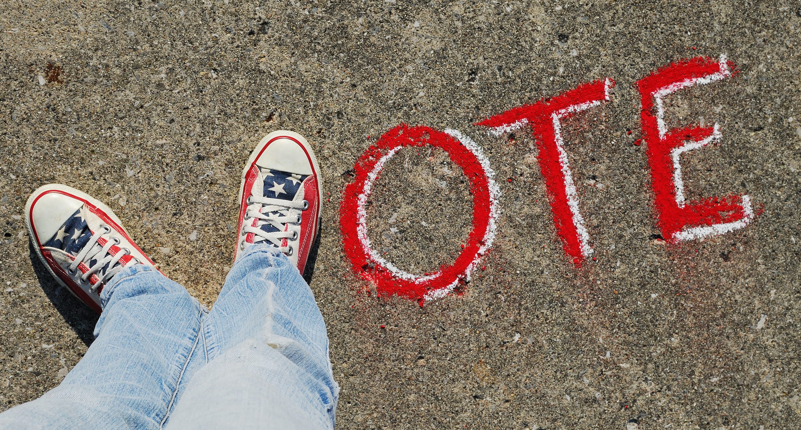 The word "vote" is written on the ground, with two sneakered feet used for the "v"